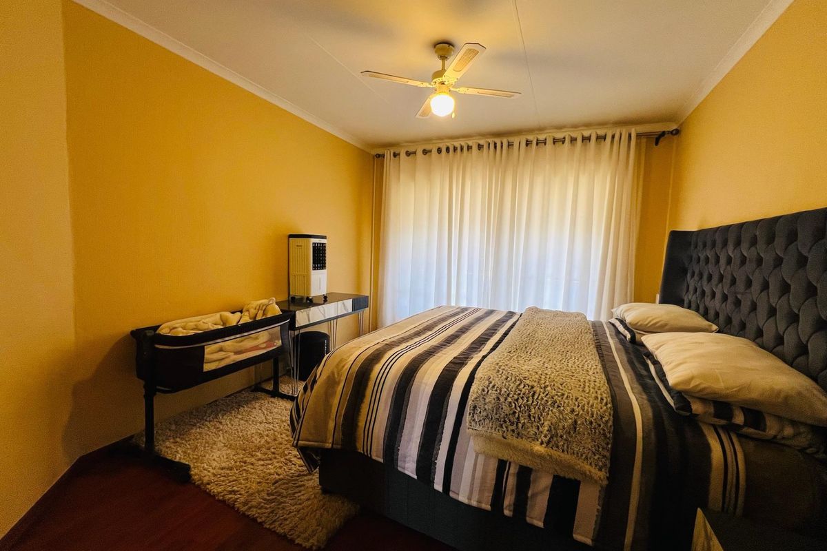 A bedroom featuring laminate flooring, a ceiling fan, and large window curtains, providing a functional space with potential for aesthetic updates.