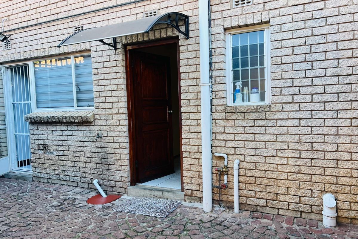 Rear exterior view of an apartment featuring a face brick facade, security gate, and paved courtyard area.