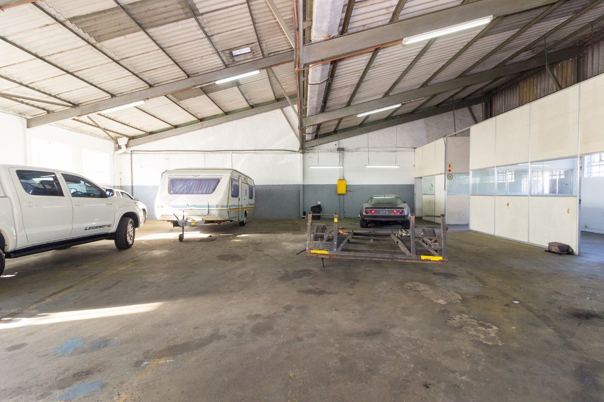 Spacious industrial garage featuring high ceilings with exposed steel trusses, concrete flooring, and an integrated partitioned office area.