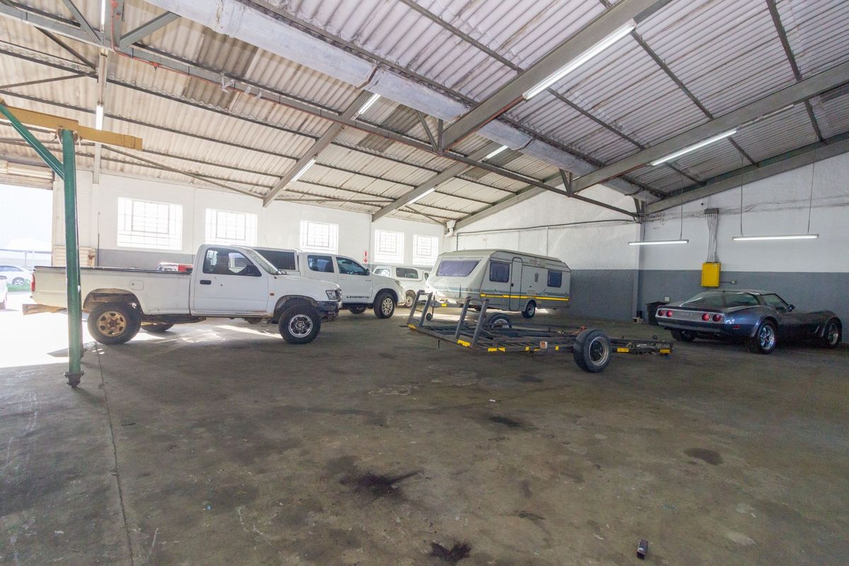 Spacious industrial garage featuring high exposed steel trusses, concrete flooring, and ample overhead fluorescent lighting, suitable for vehicle storage or workshop use.