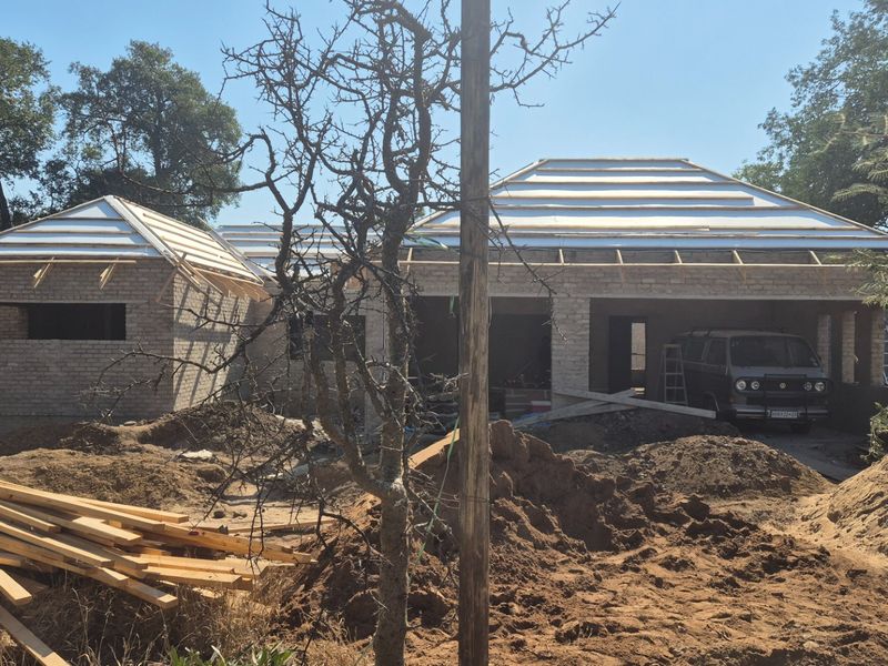 A residential property currently under construction, featuring exposed brickwork and roof trusses on a site undergoing active development.