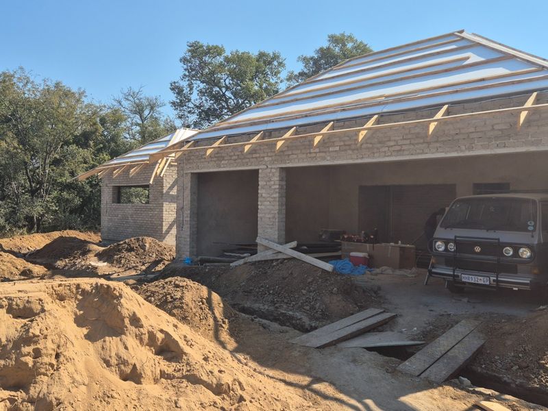 A construction-phase garage structure featuring exposed brickwork and roof trusses, currently in the early stages of development.