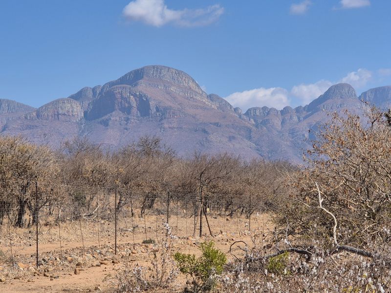 A scenic view of rugged mountain ranges overlooking a dry, natural landscape with a wire boundary fence in the foreground.