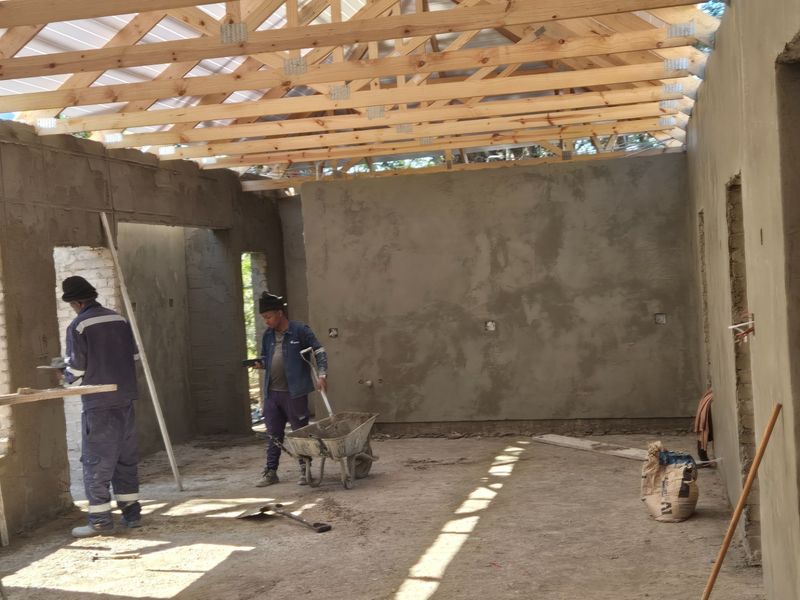 An open-plan interior space currently under construction, featuring exposed timber roof trusses and freshly plastered masonry walls.