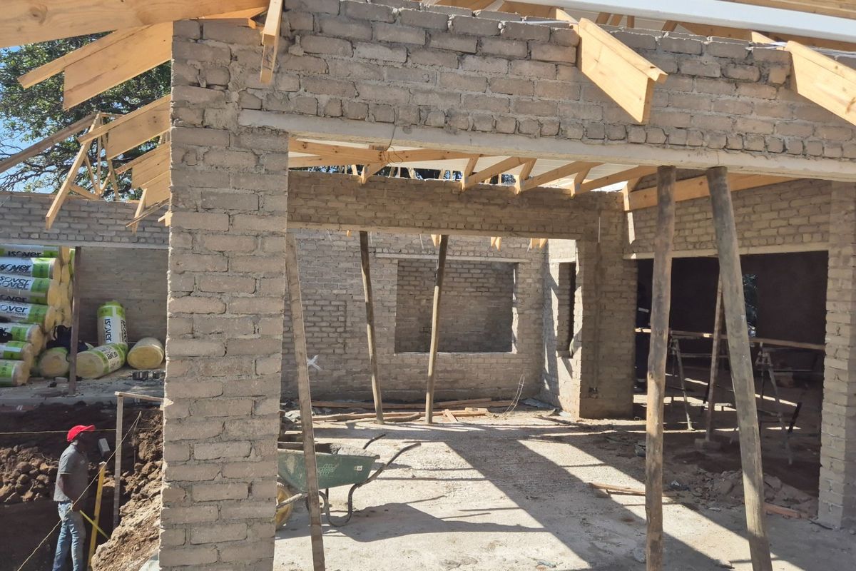 A property under construction showing exposed brick walls and timber roof trusses, indicating an ongoing building project.
