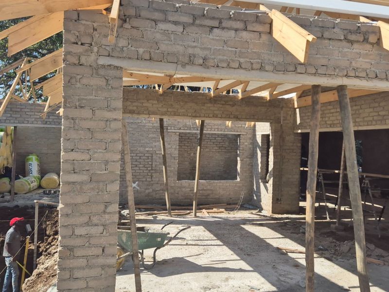 A property under construction showing exposed brick walls and timber roof trusses, indicating an ongoing building project.