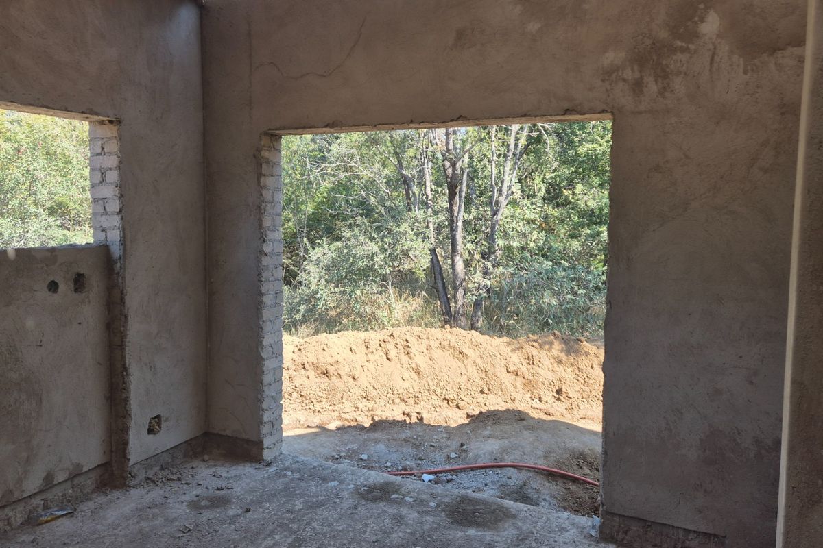 An unfinished interior space under construction featuring raw plastered walls, concrete flooring, and large openings leading to the exterior.
