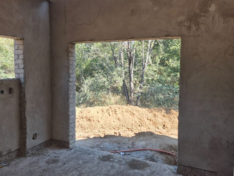 An unfinished interior space under construction featuring raw plastered walls, concrete flooring, and large openings leading to the exterior.