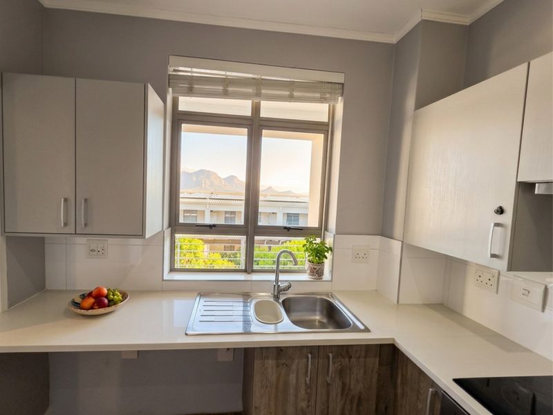 A modern kitchen featuring quartz countertops, stainless steel sink, and ample cabinetry, with a window offering pleasant mountain views.
