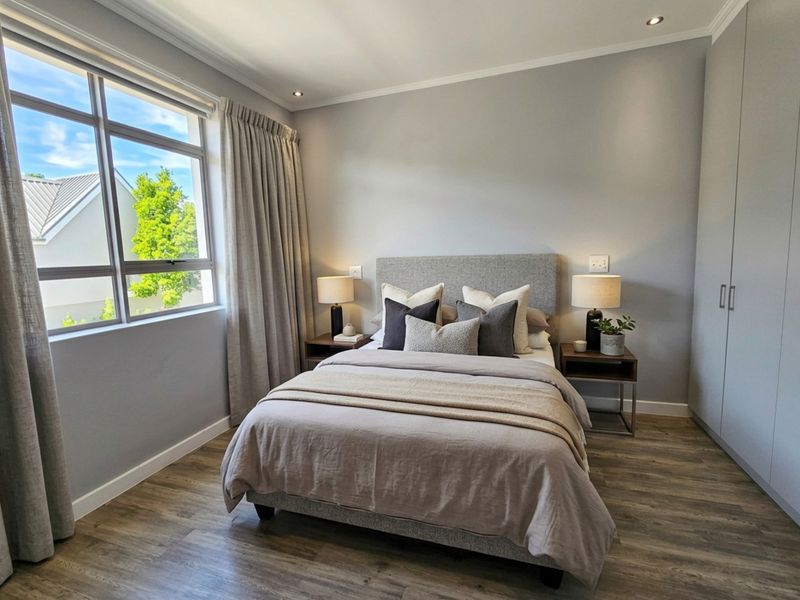 A well-maintained bedroom featuring modern laminate flooring, built-in cupboards, recessed downlighting, and large windows allowing for ample natural light.