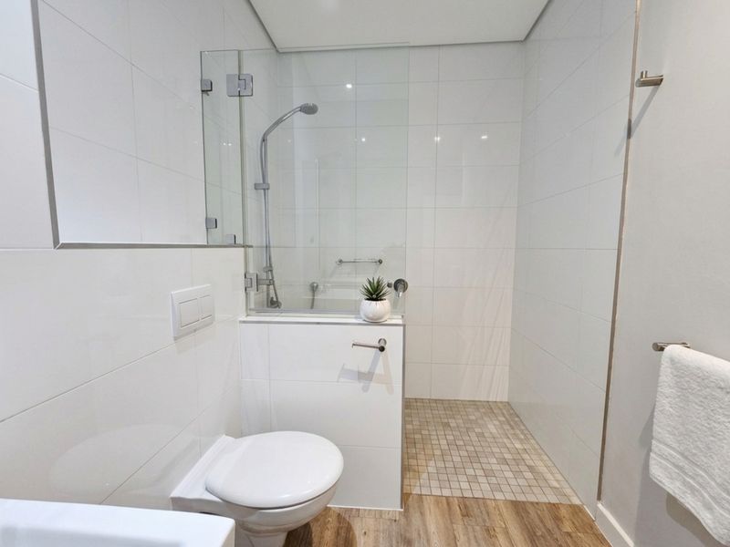 Modern bathroom featuring a wall-mounted toilet, glass shower enclosure with tiled base, and clean white wall tiling.
