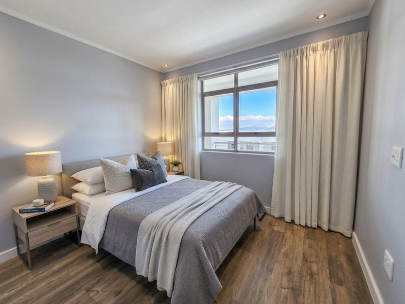 A well-maintained bedroom featuring modern laminate flooring, recessed downlighting, and a large window with natural light and scenic views.
