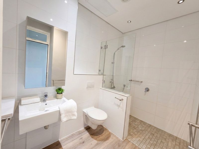 Modern bathroom featuring a wall-mounted basin, wall-hung toilet, and a spacious walk-in shower with a glass screen and neutral tiling.