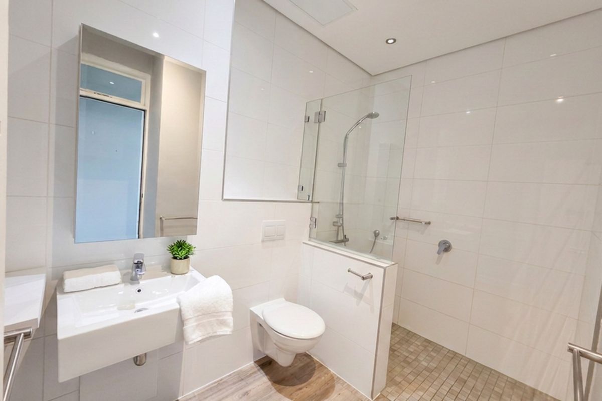 Modern bathroom featuring a wall-mounted basin, wall-hung toilet, and a spacious walk-in shower with a glass screen and neutral tiling.