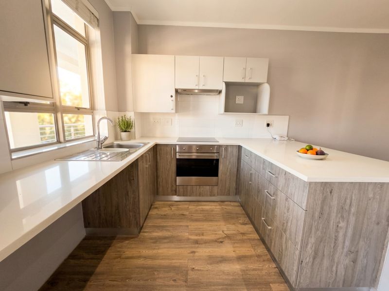 Modern kitchen featuring wood-look cabinetry, white quartz countertops, integrated stainless steel appliances, and durable laminate flooring with ample natural light.