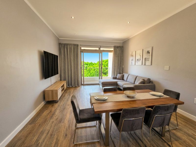 Open-plan living and dining area featuring laminate flooring, recessed lighting, and direct access to a private balcony through sliding glass doors.