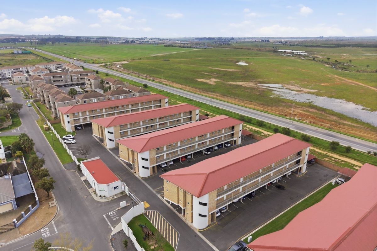 Aerial view of a multi-story apartment complex featuring red metal roofs, paved parking areas, and a secure gated entrance.