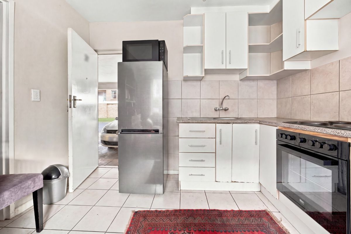 Compact kitchen featuring white built-in cabinetry, tiled backsplash, integrated oven and hob, and tiled flooring with direct access to the exterior.