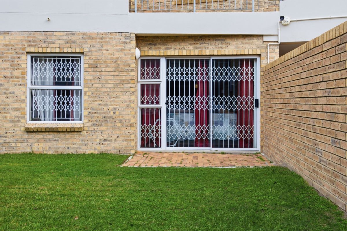 Rear view of the apartment featuring a brick facade, sliding glass door with security gate, and a small private lawn area.