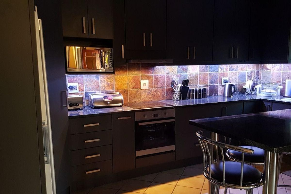 Modern kitchen featuring dark cabinetry, granite countertops, stone tile backsplash, and integrated appliances with under-cabinet lighting.