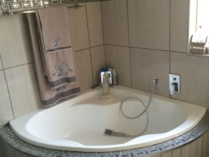A bathroom featuring a built-in corner bathtub with mosaic tile detailing and a handheld shower mixer.