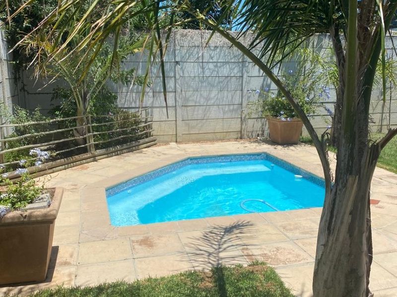 Outdoor pool area featuring a paved surround, established garden elements, and secure boundary walling.