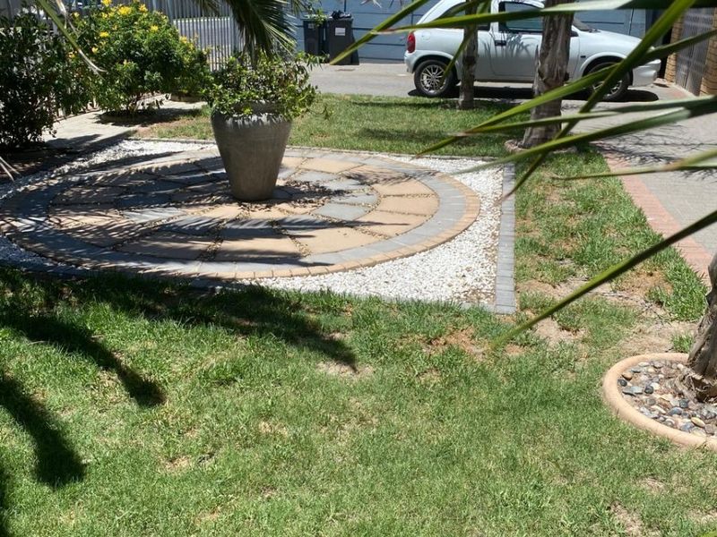 A well-maintained garden area featuring a decorative circular paved feature, established lawn, and mature palm trees.