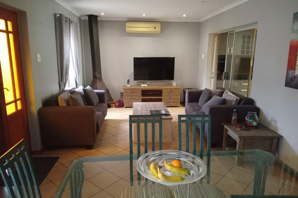 A comfortable living room featuring tiled flooring, a built-in fireplace, and an air conditioning unit, with direct access to adjacent spaces via sliding glass doors.