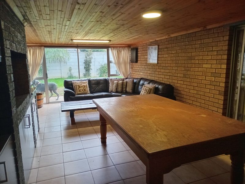Enclosed patio area featuring a built-in braai, tiled flooring, and exposed timber ceiling, with sliding glass doors providing access to the rear garden.