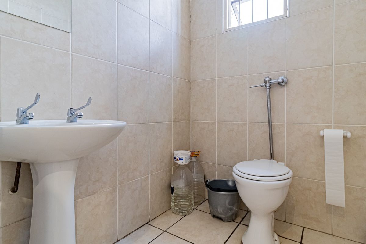 A functional bathroom featuring a pedestal basin, flush valve toilet, and neutral ceramic tiling throughout.