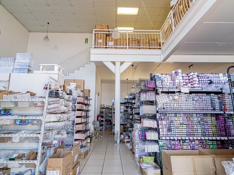 Commercial retail or storage space featuring a mezzanine level with metal staircase, tiled flooring, and extensive built-in shelving units.