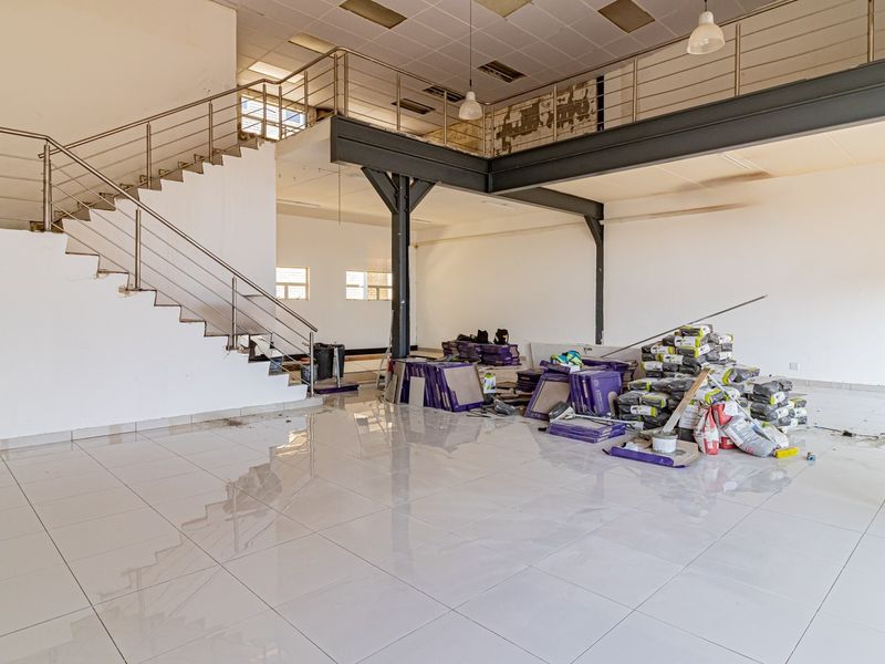 Spacious open-plan commercial unit featuring a mezzanine level, steel staircase, tiled flooring, and industrial-style support columns, currently undergoing renovation.
