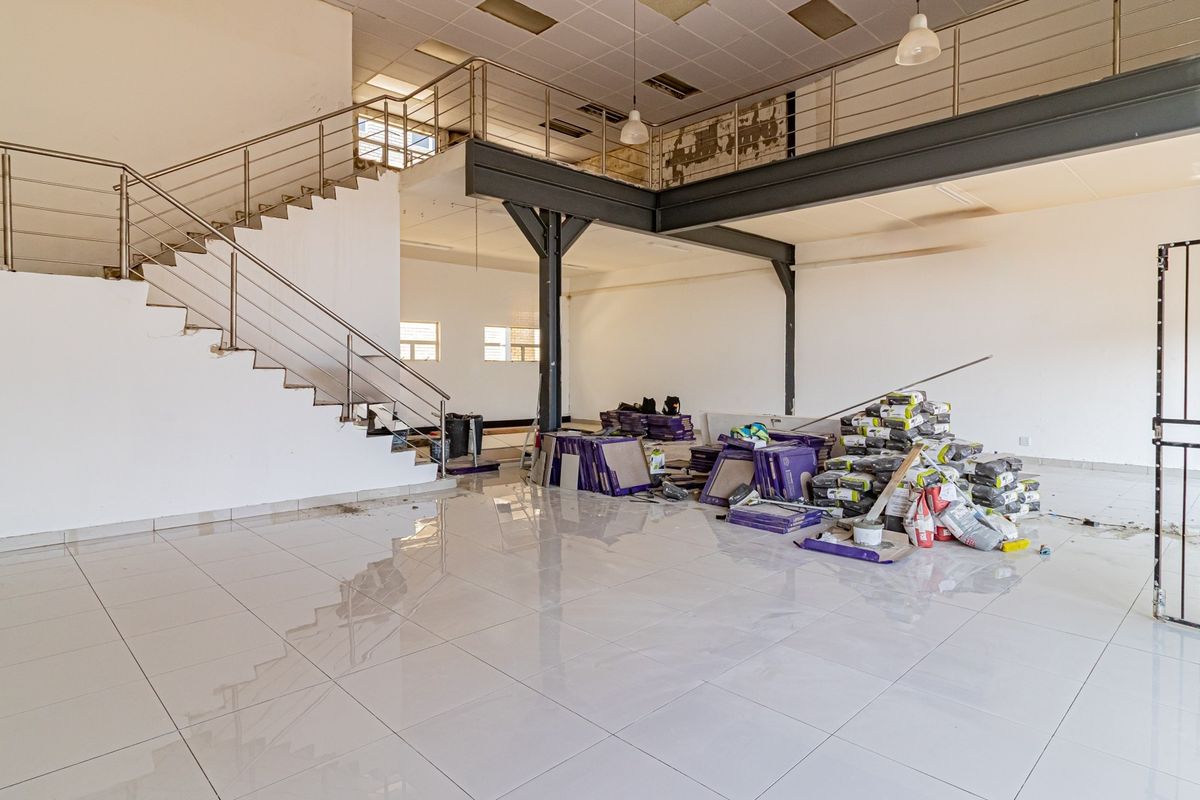 Spacious open-plan commercial unit featuring a mezzanine level, steel staircase, tiled flooring, and industrial-style support columns, currently undergoing renovation.