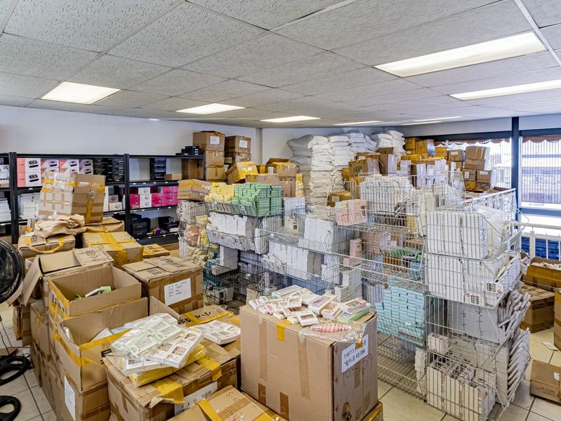 A commercial utility or storage space featuring a suspended ceiling with recessed lighting and tiled flooring, currently utilized for inventory storage.