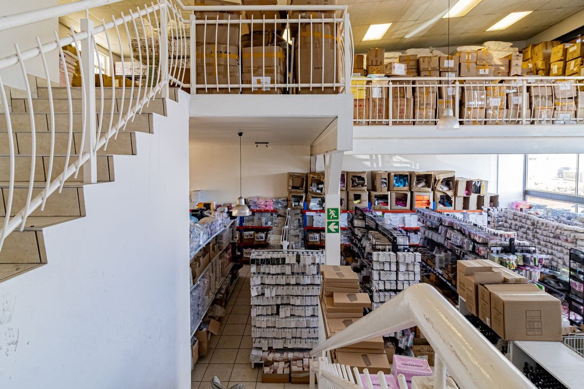 Commercial warehouse space featuring a mezzanine level, metal staircase, and tiled flooring, currently utilized for storage and inventory management.
