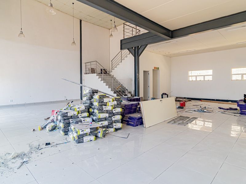 Spacious open-plan commercial unit featuring tiled floors, exposed steel structural beams, and a mezzanine staircase, currently undergoing final finishing works.