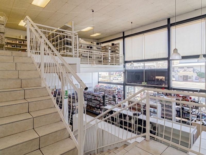 Spacious commercial retail unit featuring a mezzanine level, tiled staircase with metal balustrades, and large glass windows providing excellent natural light and street visibility.