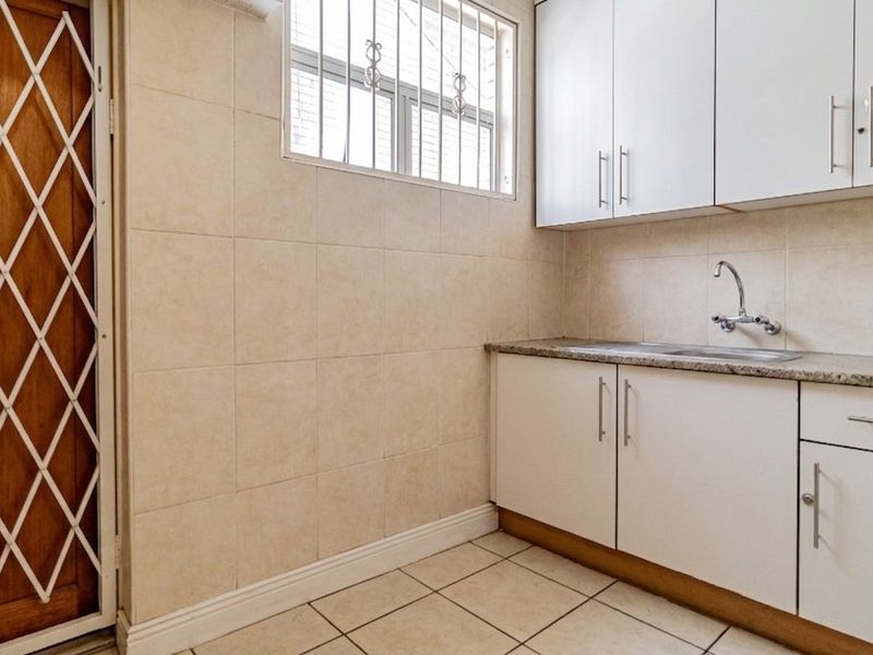 A functional scullery or utility area featuring built-in cabinetry, a stainless steel sink, tiled splashbacks, and secure access points.