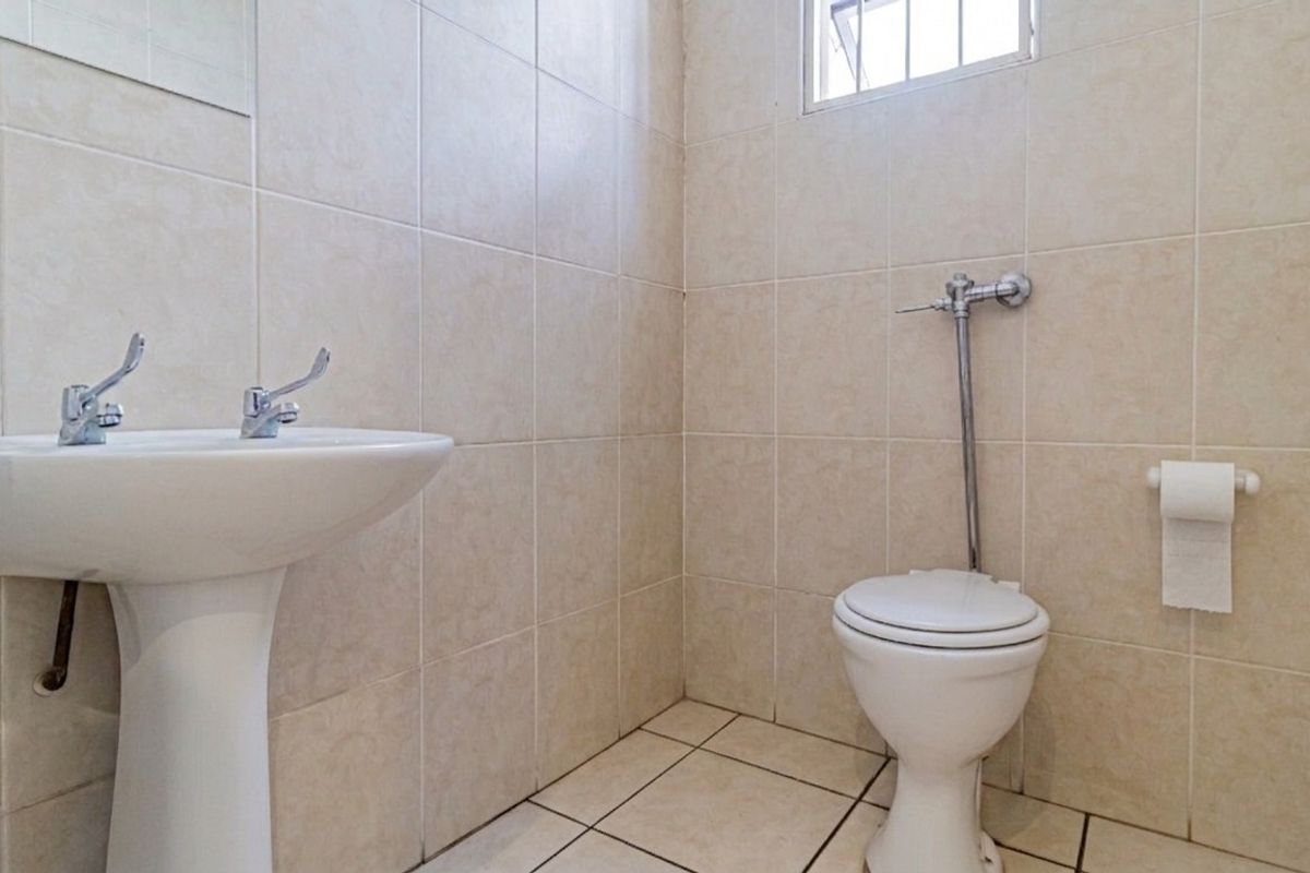 A functional commercial restroom featuring a pedestal basin, flush valve toilet, and neutral ceramic tiling throughout.