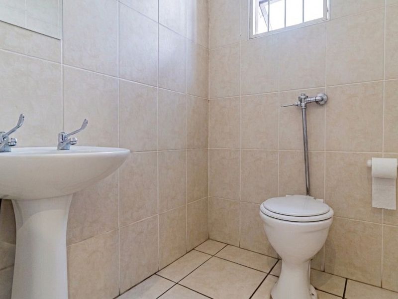 A functional commercial restroom featuring a pedestal basin, flush valve toilet, and neutral ceramic tiling throughout.