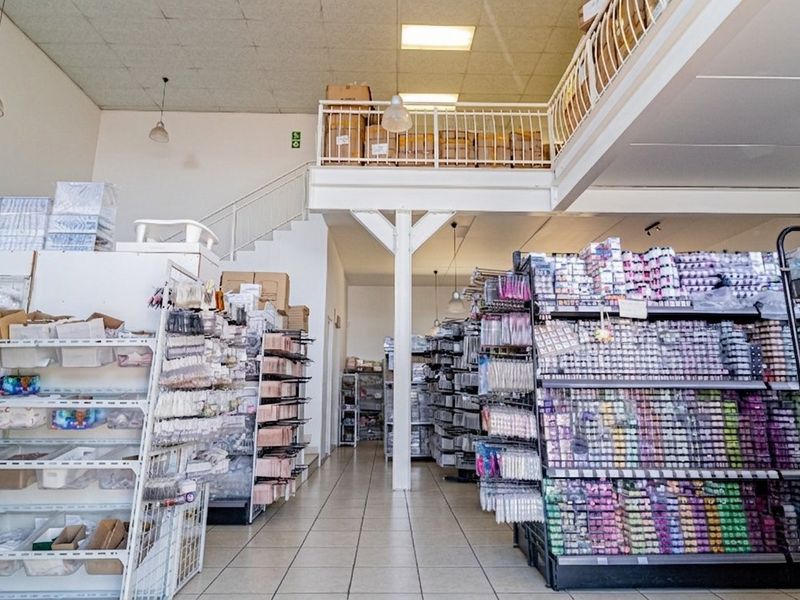 Commercial retail space featuring a mezzanine level with metal staircase, tiled flooring, and suspended ceiling with integrated lighting.