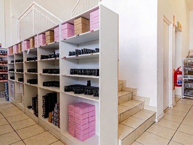 Commercial utility space featuring extensive built-in shelving units, tiled flooring, and an internal staircase with a metal balustrade.