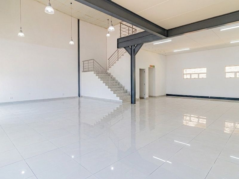 Spacious open-plan commercial unit featuring high ceilings, polished tiled floors, a steel staircase, and modern industrial lighting throughout.