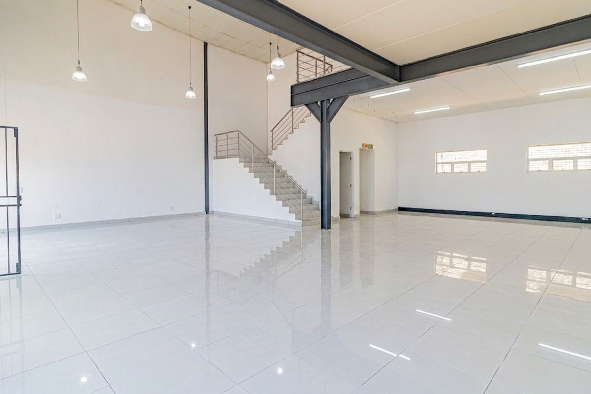 Spacious open-plan commercial unit featuring high ceilings, polished tiled floors, a steel staircase, and modern industrial lighting throughout.