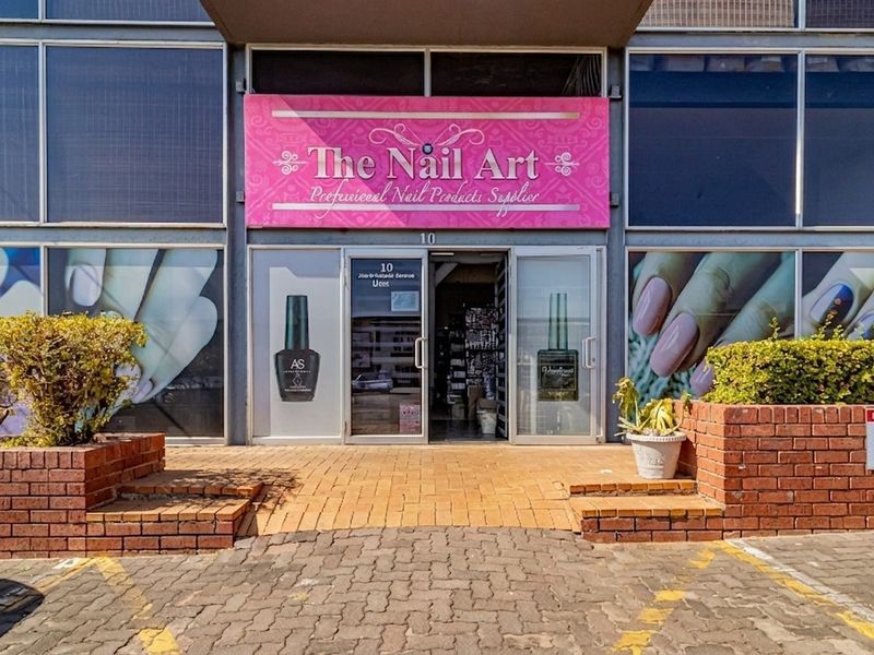 Commercial storefront entrance featuring brick planter boxes, paved approach, and large glass display windows with prominent signage.
