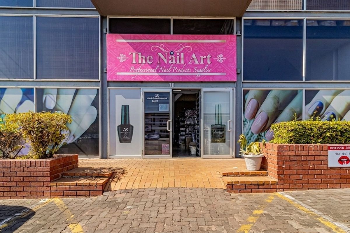 Commercial storefront entrance featuring brick planter boxes, paved approach, and large glass display windows with prominent signage.