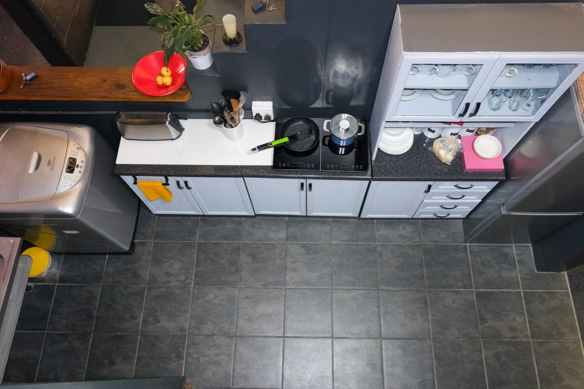 A compact, functional kitchen featuring built-in cabinetry, an electric cooktop, a stainless steel sink, and dark tiled flooring in an industrial-style setting.