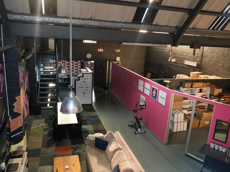 Spacious industrial open-plan area featuring exposed steel trusses, painted block walls, epoxy flooring, and partitioned office sections with high ceilings.