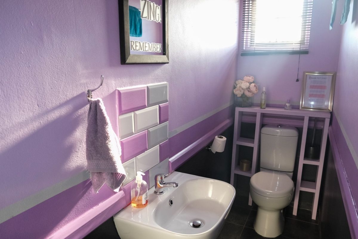 A compact bathroom featuring a white toilet, modern washbasin with chrome faucet, and decorative purple and grey wall tiling.