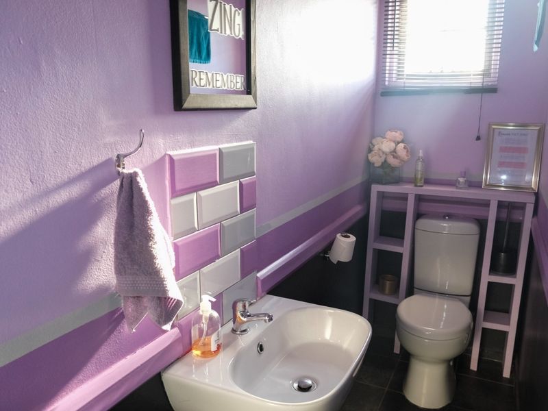 A compact bathroom featuring a white toilet, modern washbasin with chrome faucet, and decorative purple and grey wall tiling.